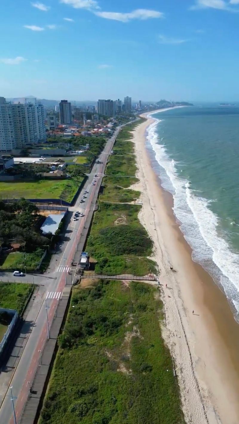 Vista aérea de drone da orla de Balneário Piçarras, com a praia, a vegetação de restinga e a avenida beira-mar